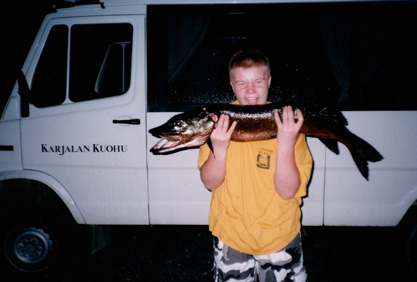 Boy holding a large pike in front of the Karjalan Kuohu van
