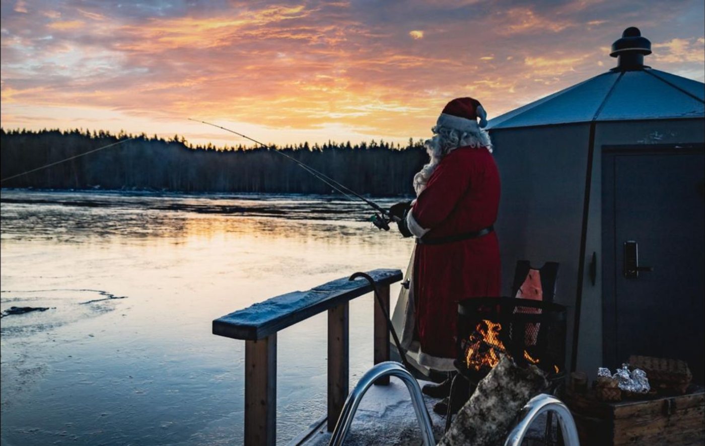 Santa Claus fishing from the deck of a heated ice-fishing hut at sunrise